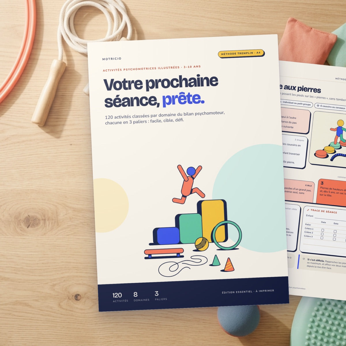 Couverture de Motricio Essentiel imprimée sur une table, avec une corde à sauter, un cerceau et des sacs lestés